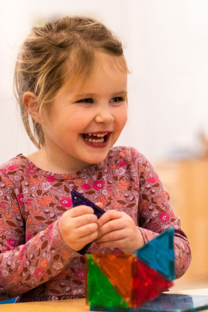 Small girl smiling while playing with a colorful puzzle